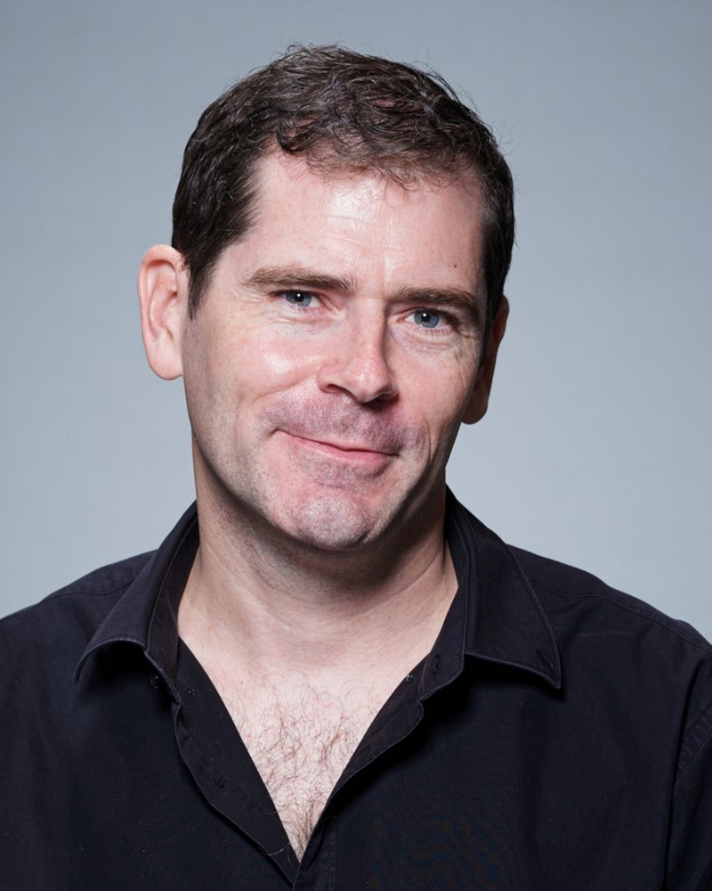 Sébastien Maleville, smiling, in a black shirt against a grey studio backdrop.