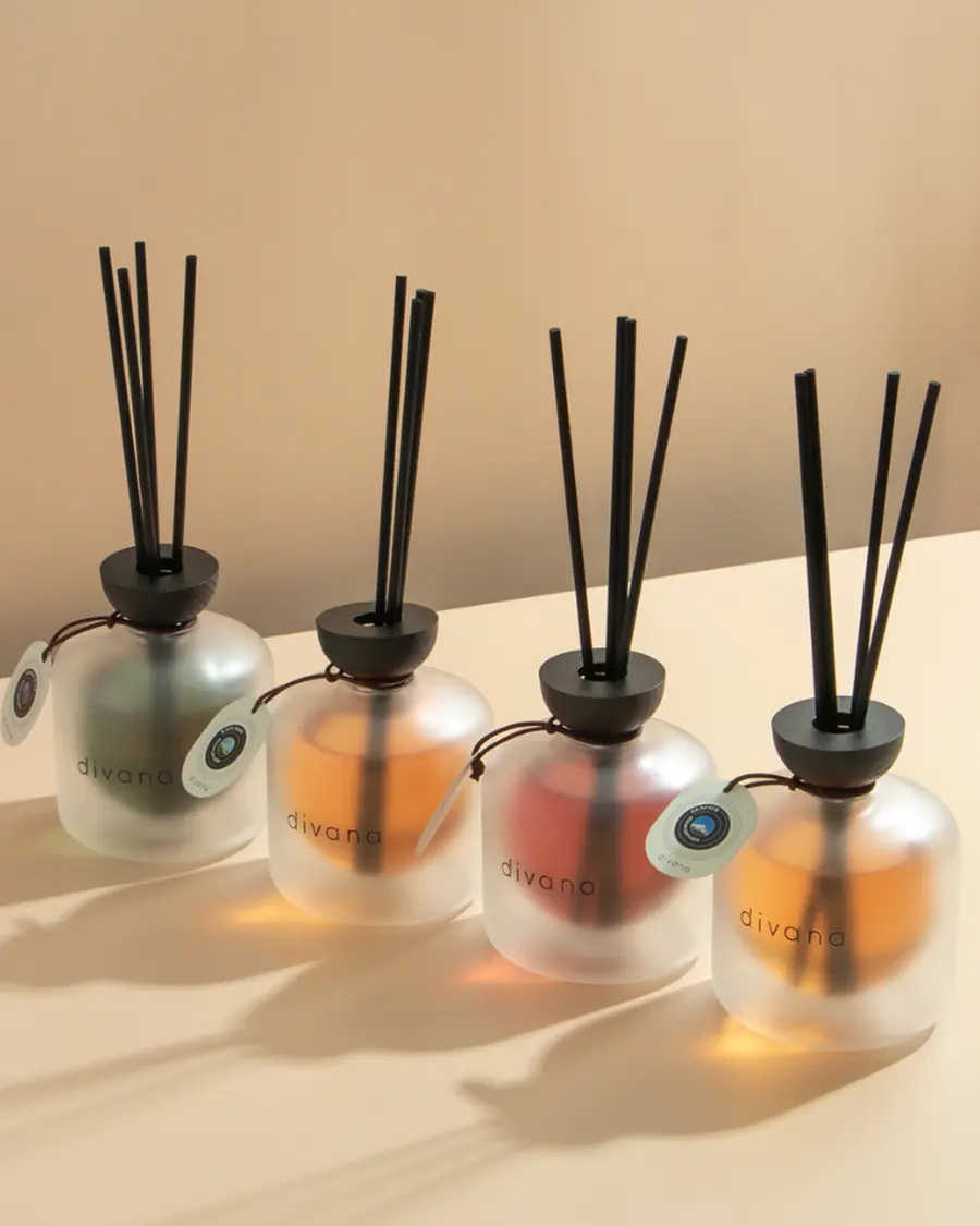 Four frosted Divana reed diffusers with black reeds on a warm beige surface.