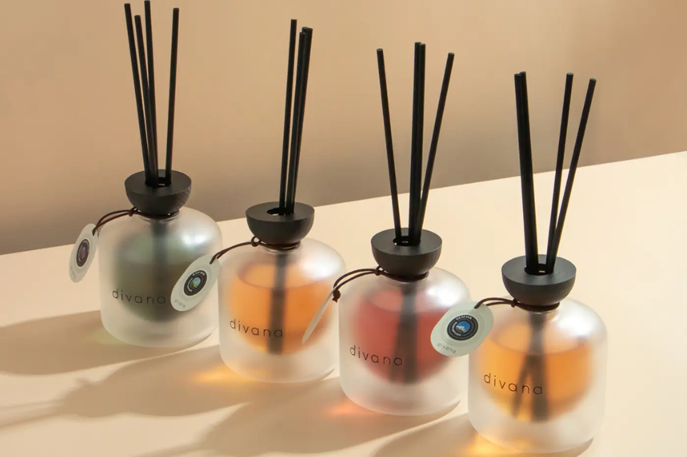 Four frosted Divana reed diffusers with black reeds on a warm beige surface.