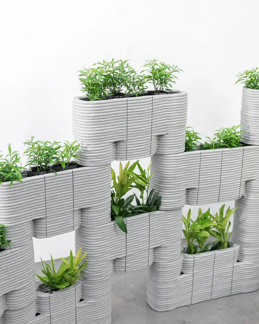 Grey 3D-printed cement planter modules stacked into a wall and planted with greenery.