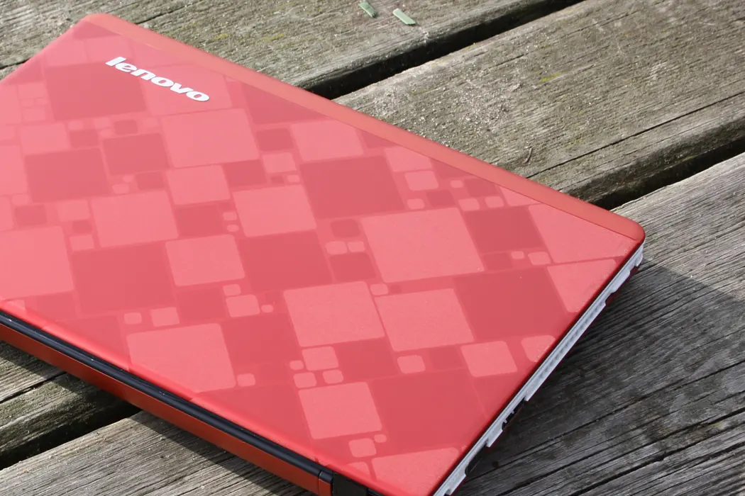 A closed Lenovo IdeaPad U160 in red on an outdoor wooden deck, its slim edge showing the book-like profile.