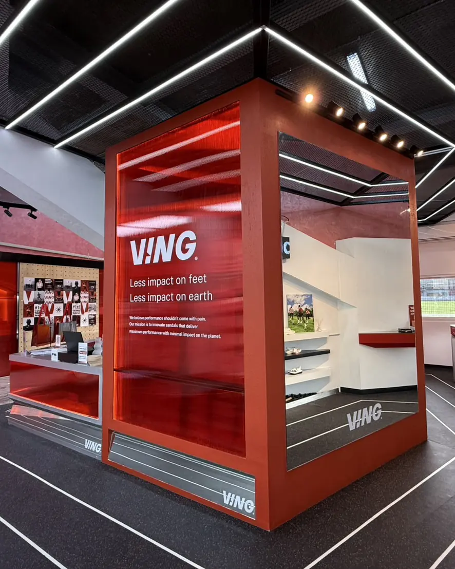 Inside the VING flagship store: a red glass cube with the line "Less impact on feet, less impact on earth", over running-track floor lines.