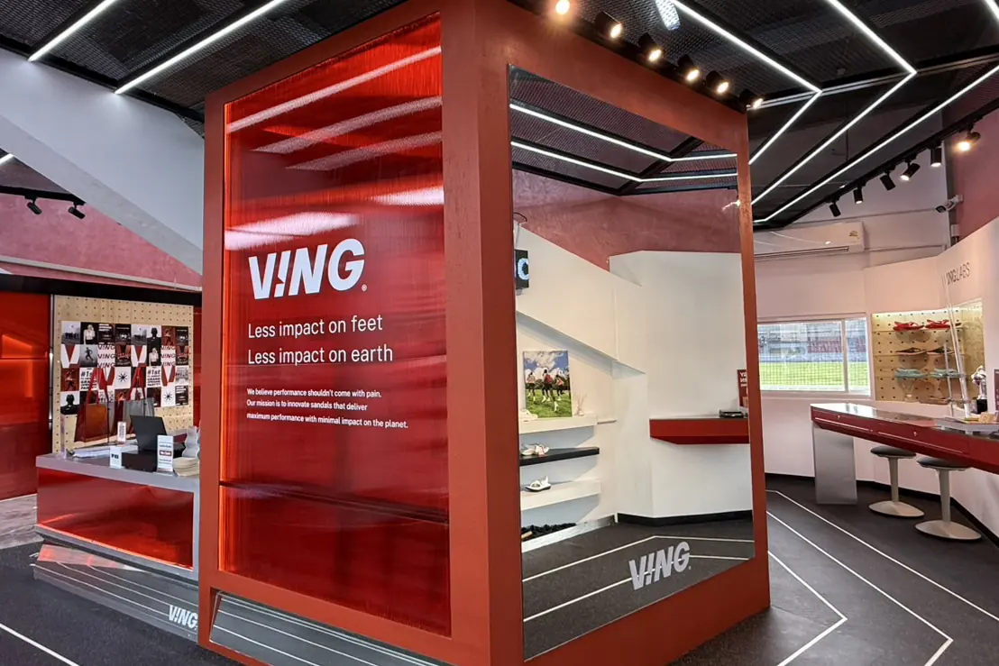 Inside the VING flagship store: a red glass cube with the line "Less impact on feet, less impact on earth", over running-track floor lines.