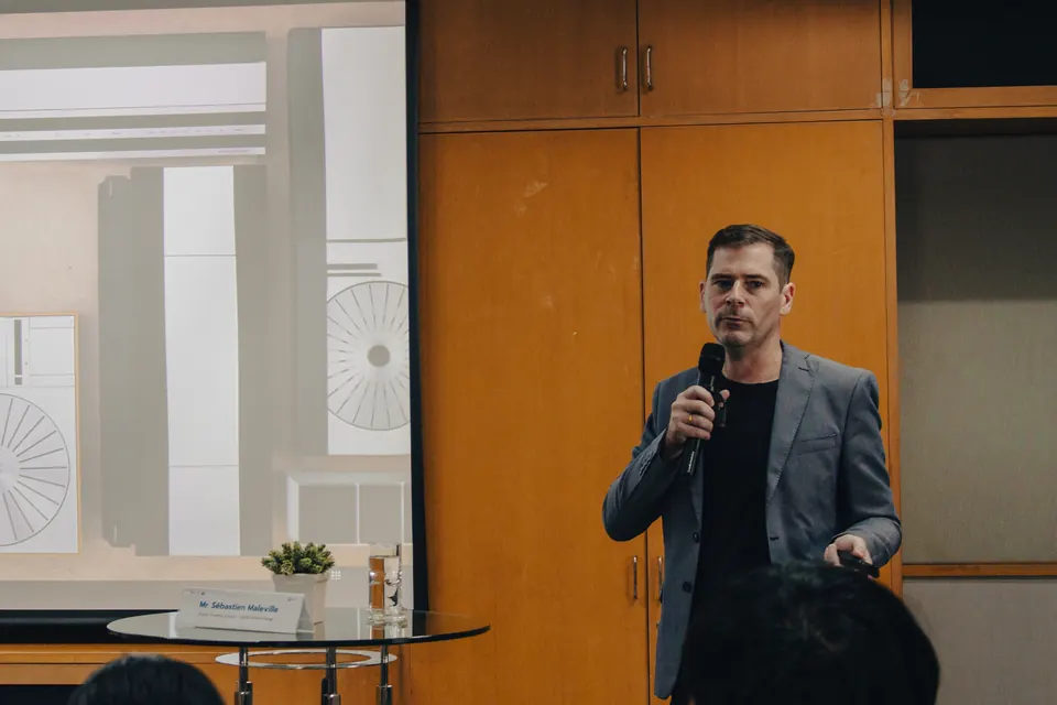 Sébastien speaking into a microphone beside a projected slide in a seminar room.