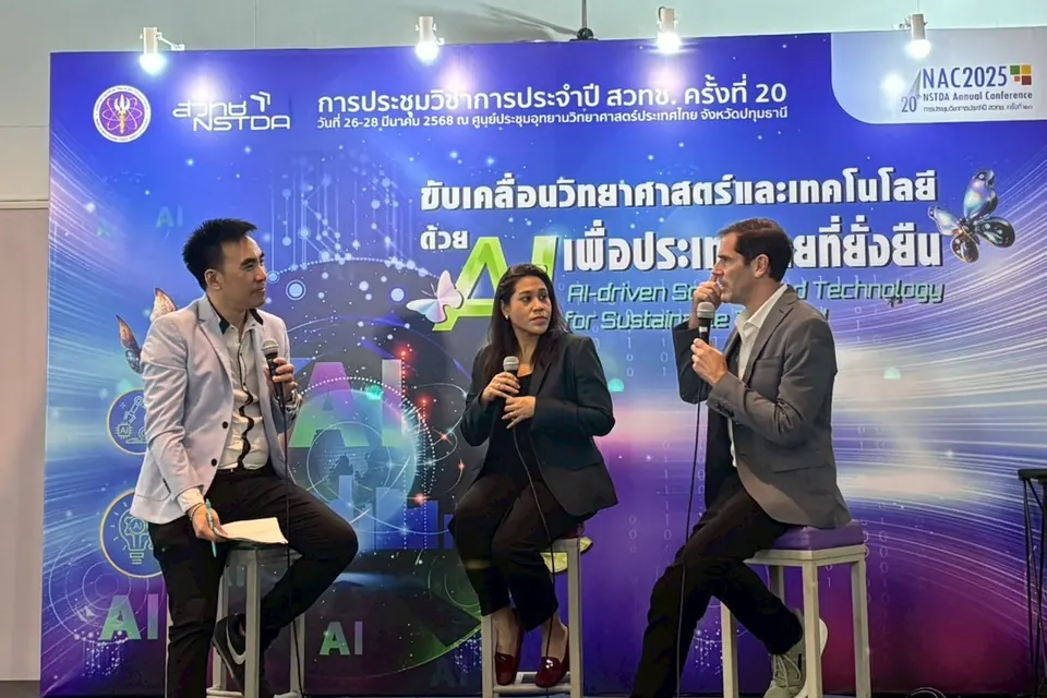 Sébastien on a stool with a microphone, the third speaker in a panel in front of the NSTDA Annual Conference backdrop.
