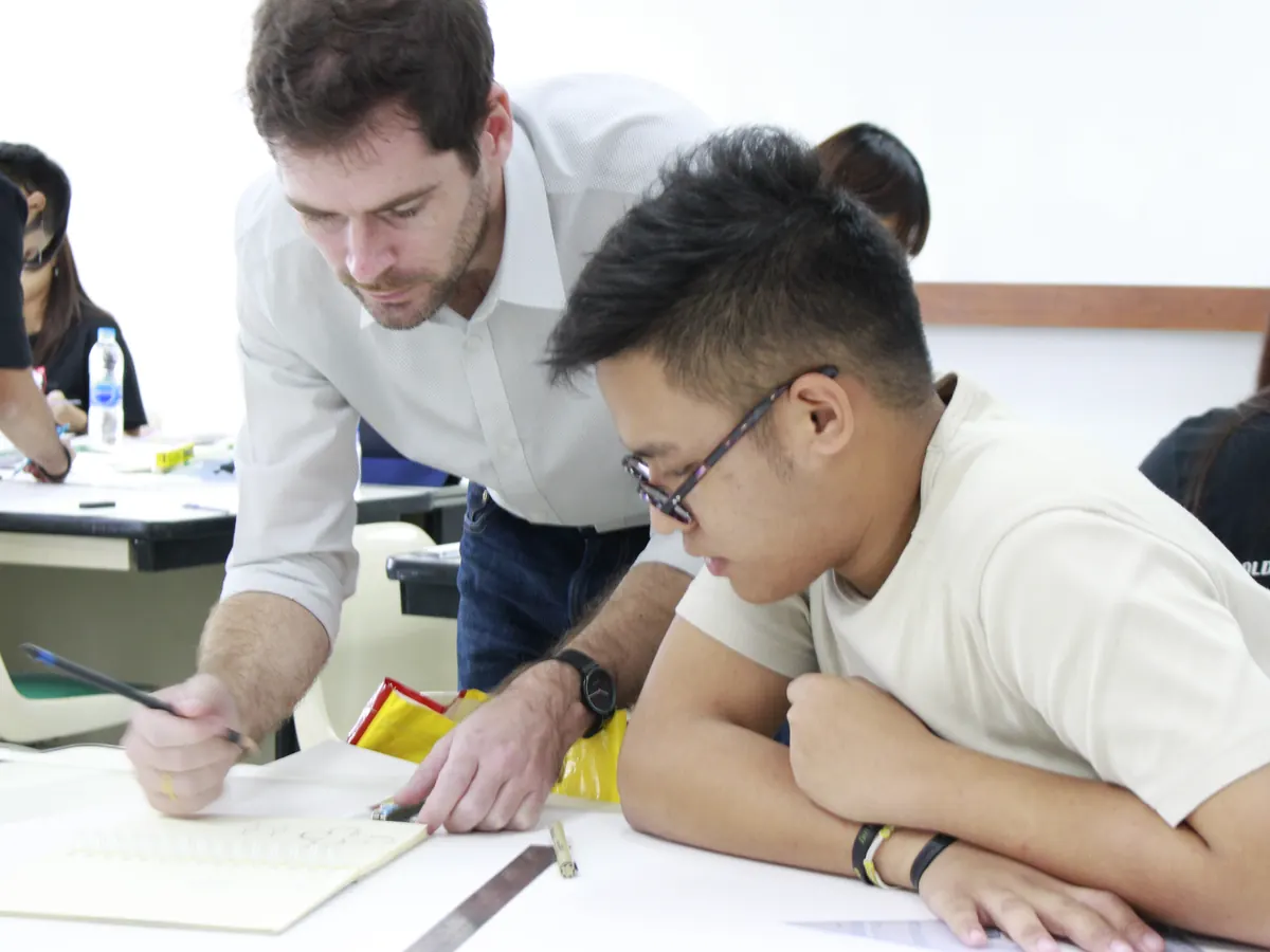 Sébastien leaning over a student's sketchbook with a pencil.